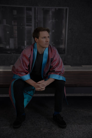 Model wearing a Burgundy coloured Kimono with botanical details (front view, model sitting), showcasing burgundy red fabric, turquoise blue collar, arm bands and reflections of the fabric on the inside.