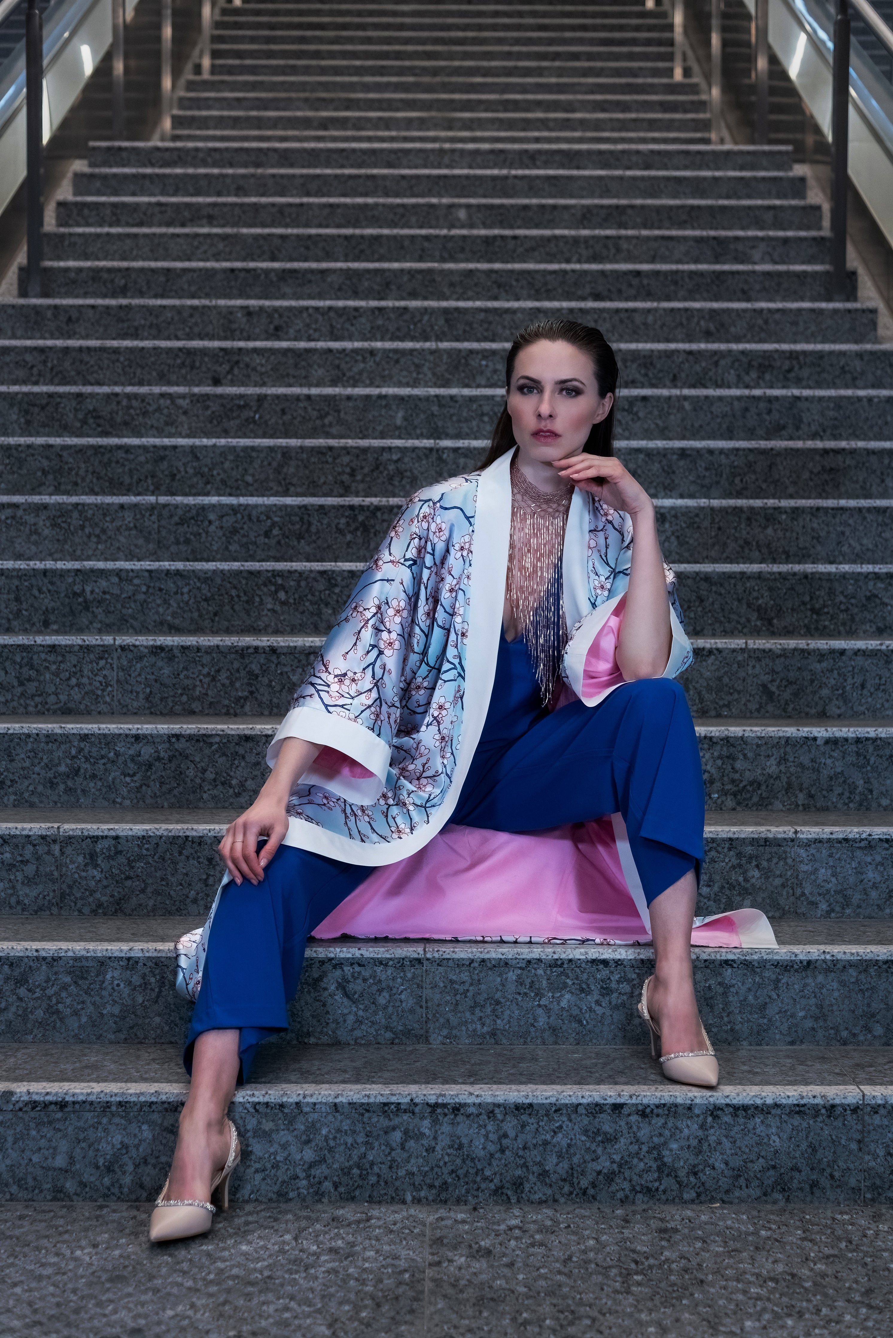 A model sits on stairs, wearing a pink kimono with a bold cherry blossom pattern visible on the outside. The pink lining shows through on the inside.