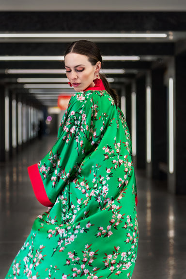 A close-up image of the kimono from the back, showcasing the delicate cherry blossom pattern against the vibrant green mulberry silk background.