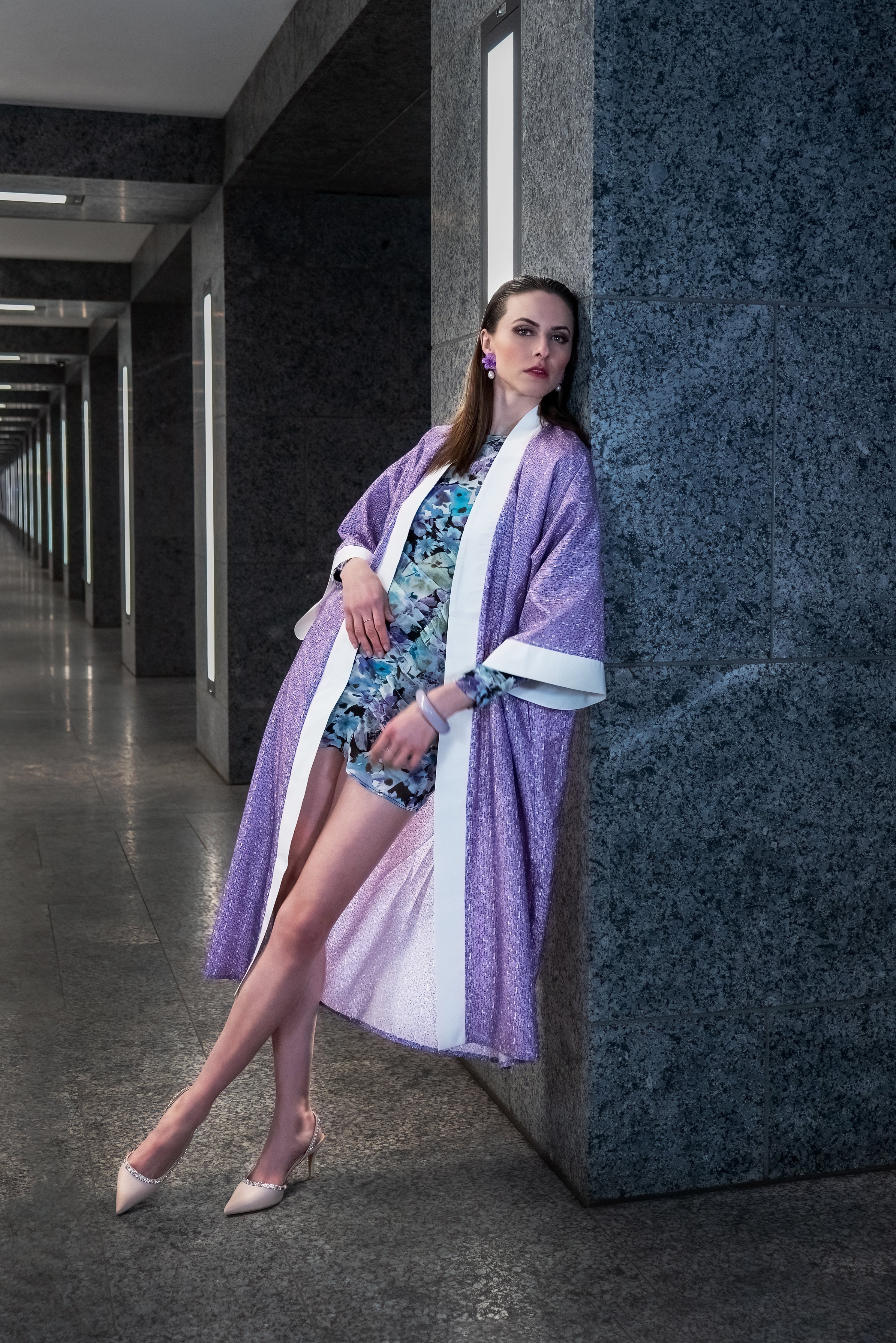 Model leaning against the wall, wearing a beautiful silk kimono with delicate lilac-hued elephant motifs, with a white collar and arm wrists.